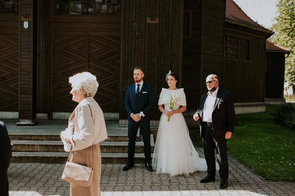 Para młoda przed kościołem, goście wokół.
