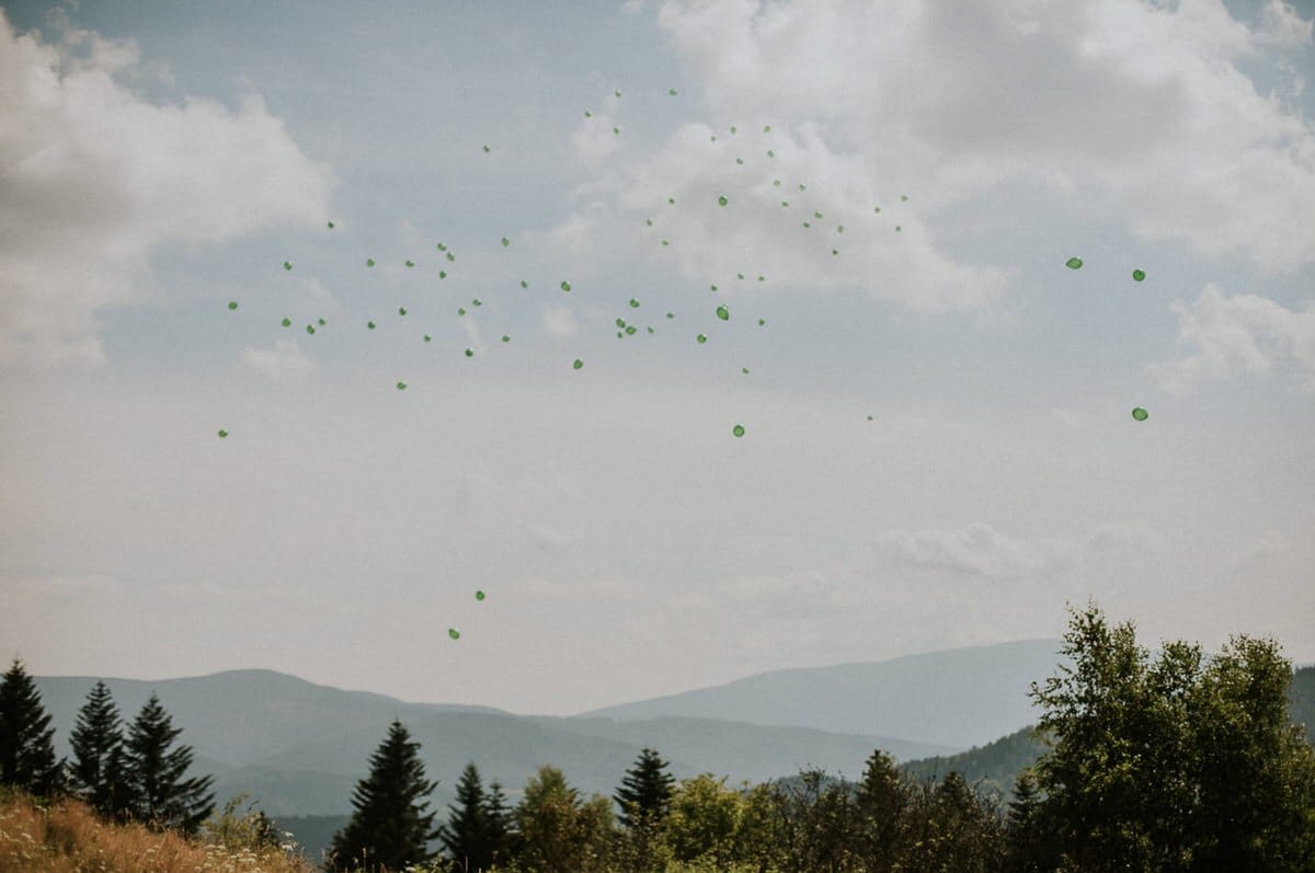 Zielone balony unoszą się nad górskim krajobrazem.