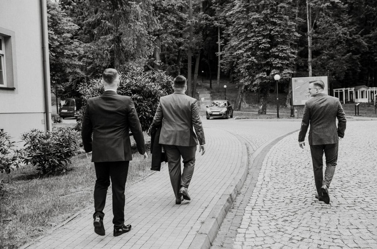 Trzech mężczyzn w garniturach idzie chodnikiem.