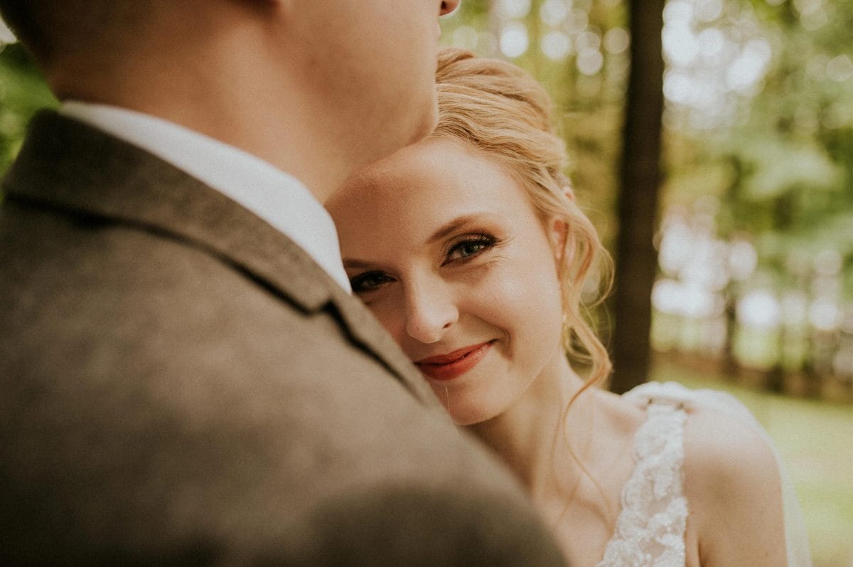 Uśmiechnięta panna młoda w plenerze, przytulona do pana młodego.