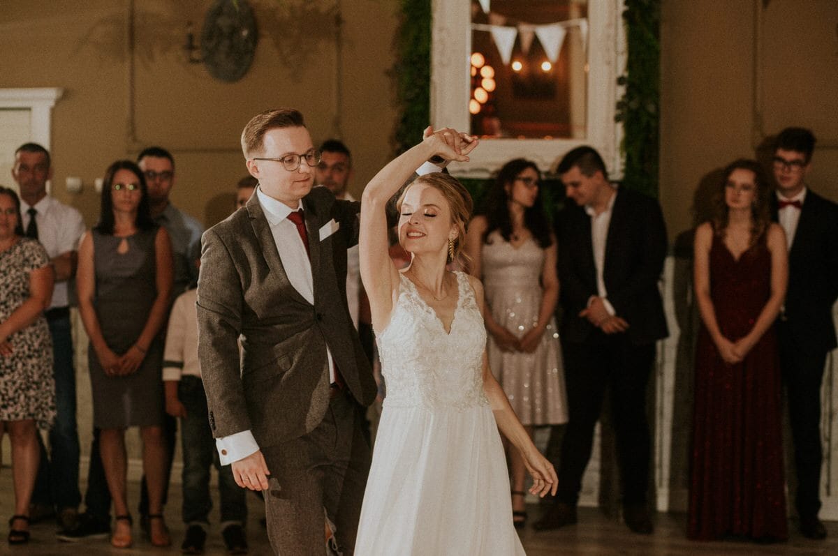 Para młoda tańczy na weselu, goście w tle.