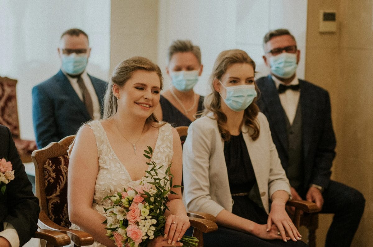 Uśmiechnięta panna młoda i goście w maskach.