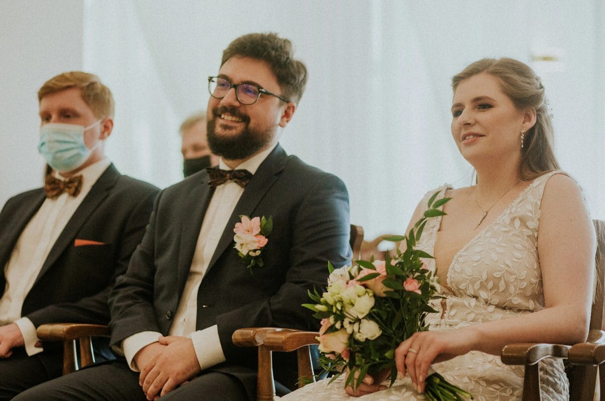 Para młoda na ceremonii ślubnej z gościem w maseczce.