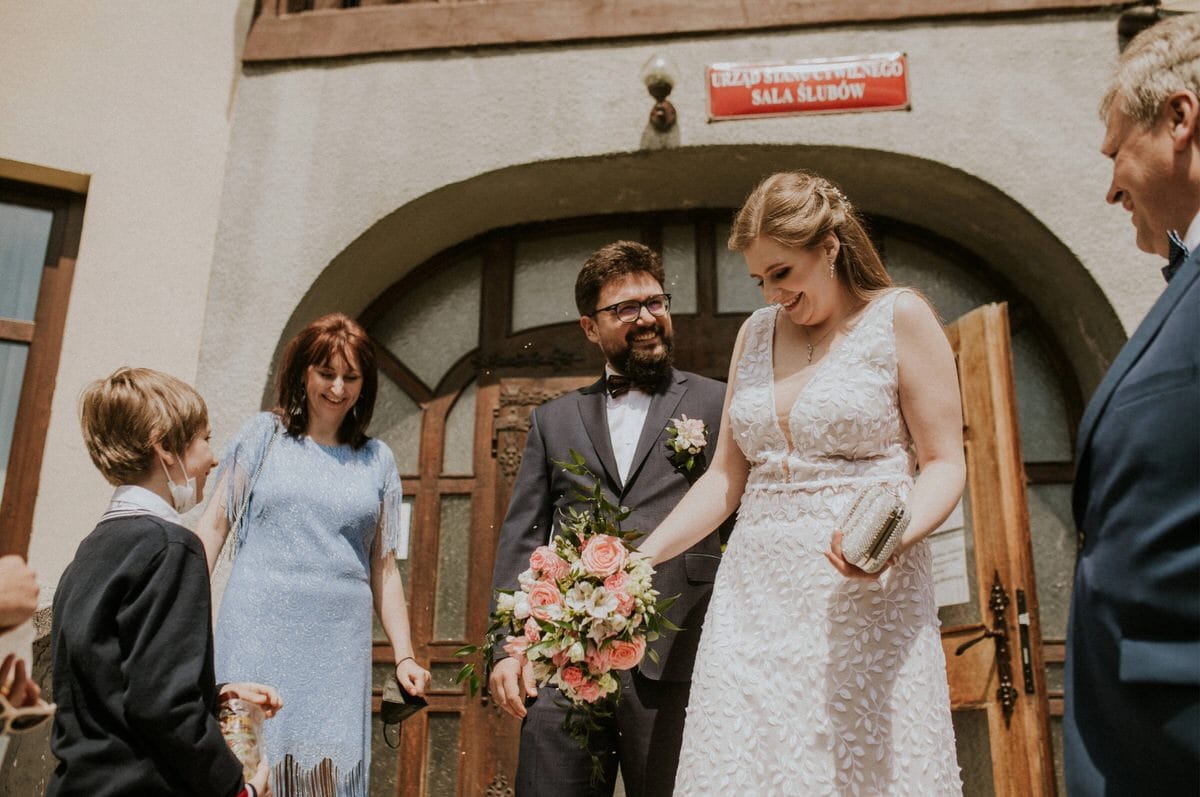 Para młoda wychodzi z urzędu ślubnego z gośćmi.