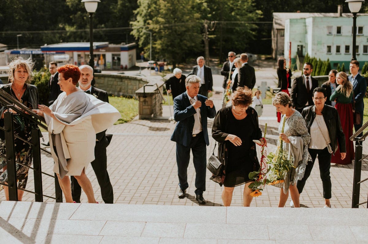 Ludzie wchodzący po schodach, trzymają kwiaty, dzień słoneczny.