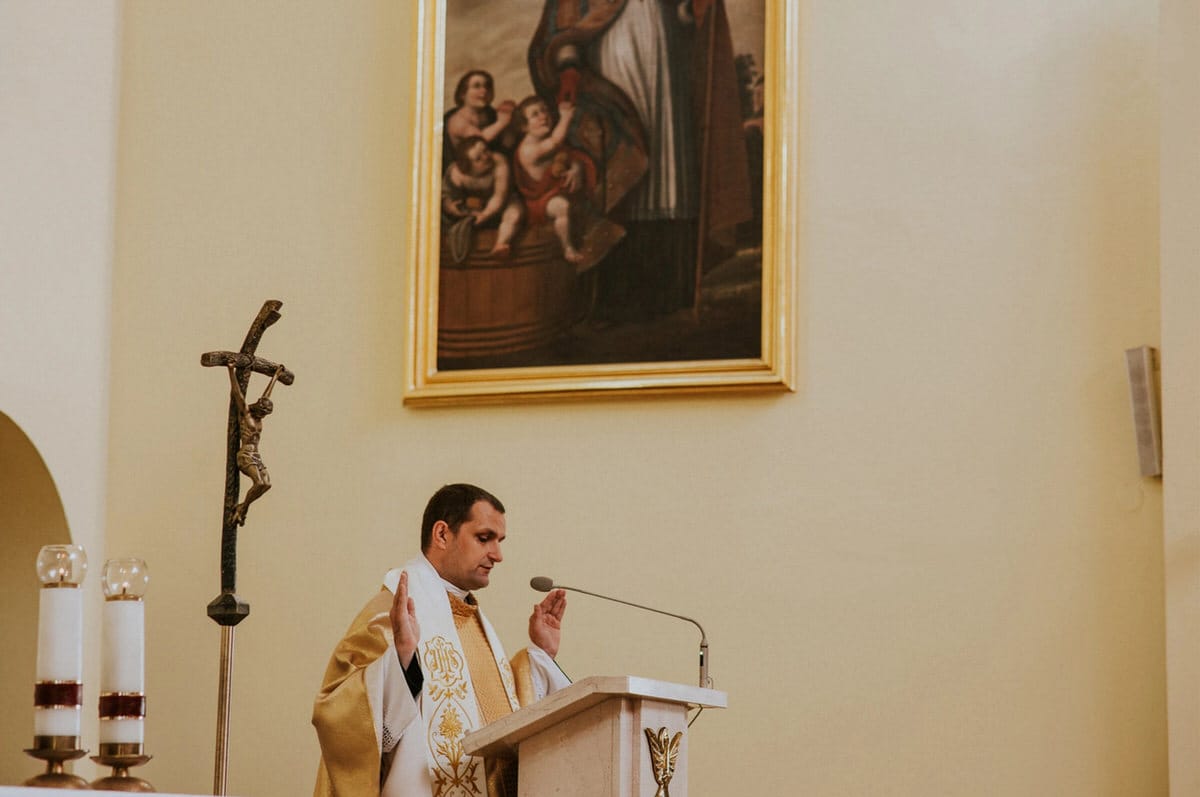 Ksiądz przy ołtarzu, obraz i krzyż w tle.