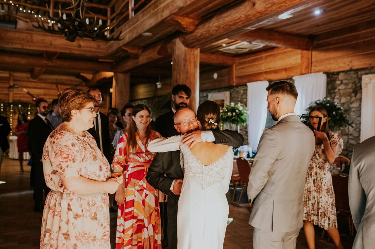 Goście weselni w drewnianej sali, przytulający się.