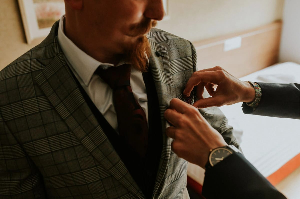 Osoba poprawia marynarkę mężczyzny w garniturze.