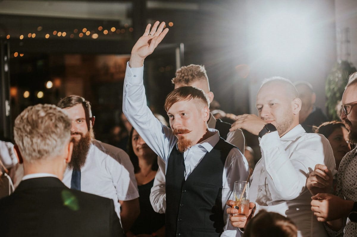 Mężczyzna z brodą wznosi rękę na przyjęciu.