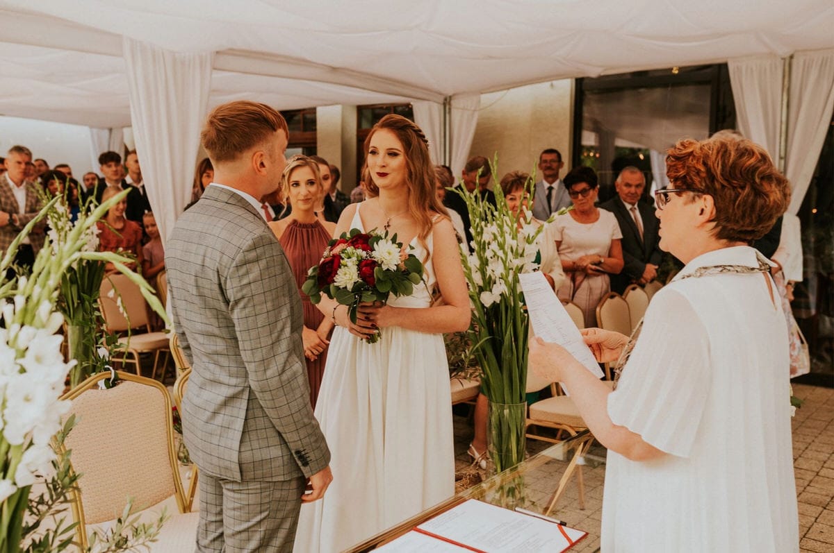 Ceremonia ślubna pary pod namiotem z gośćmi.