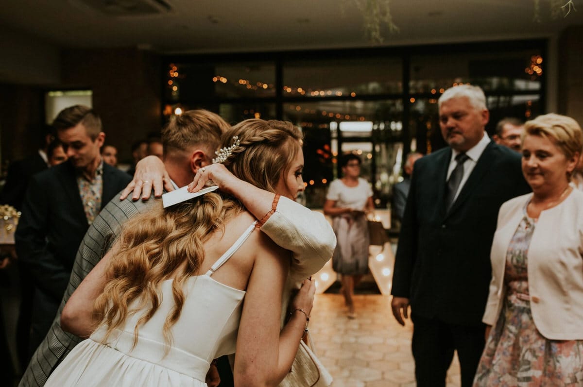 Uśmiechnięci goście na przyjęciu weselnym, przytulają się.