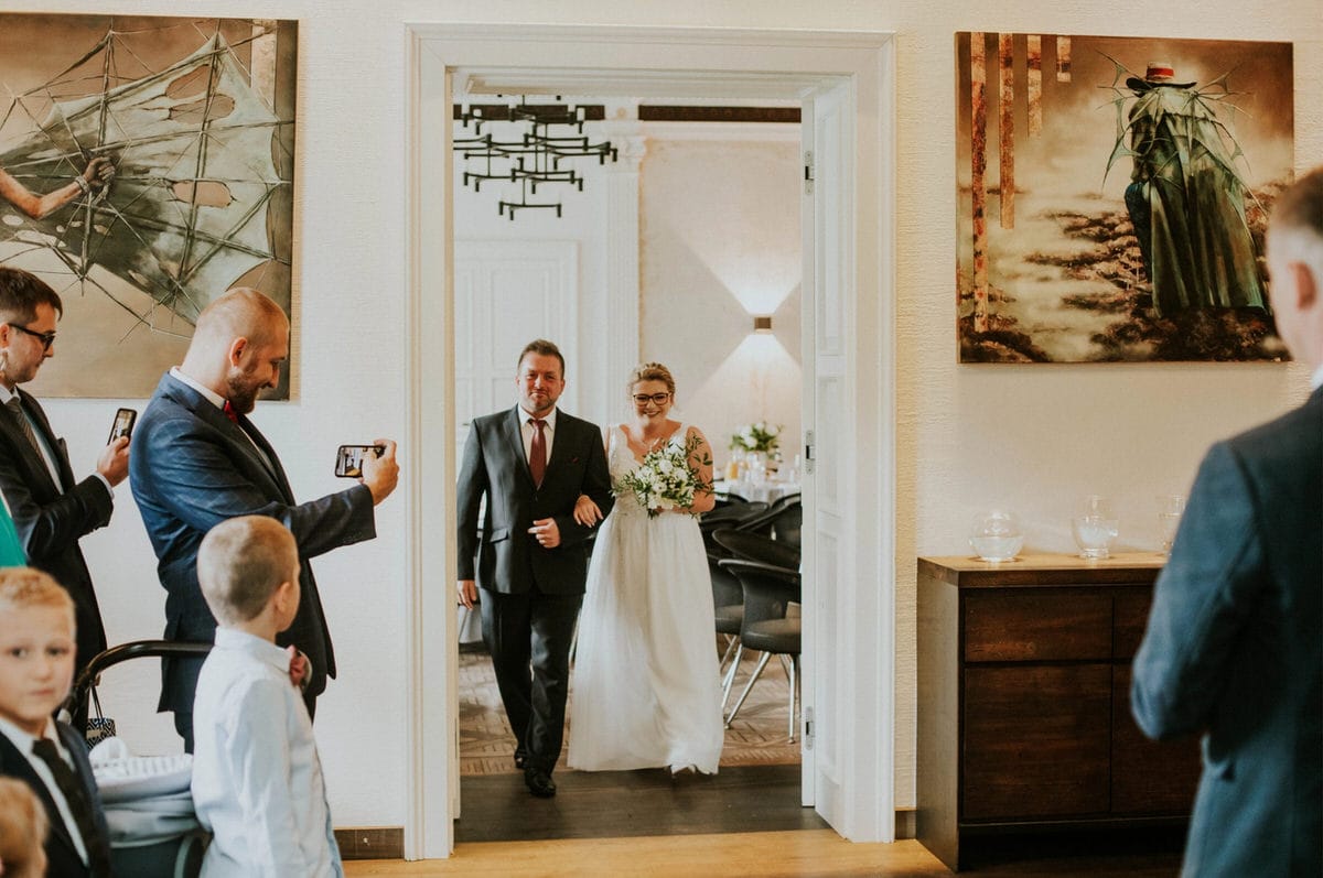 Para wchodząca na salę weselną, fotografowana przez gości.