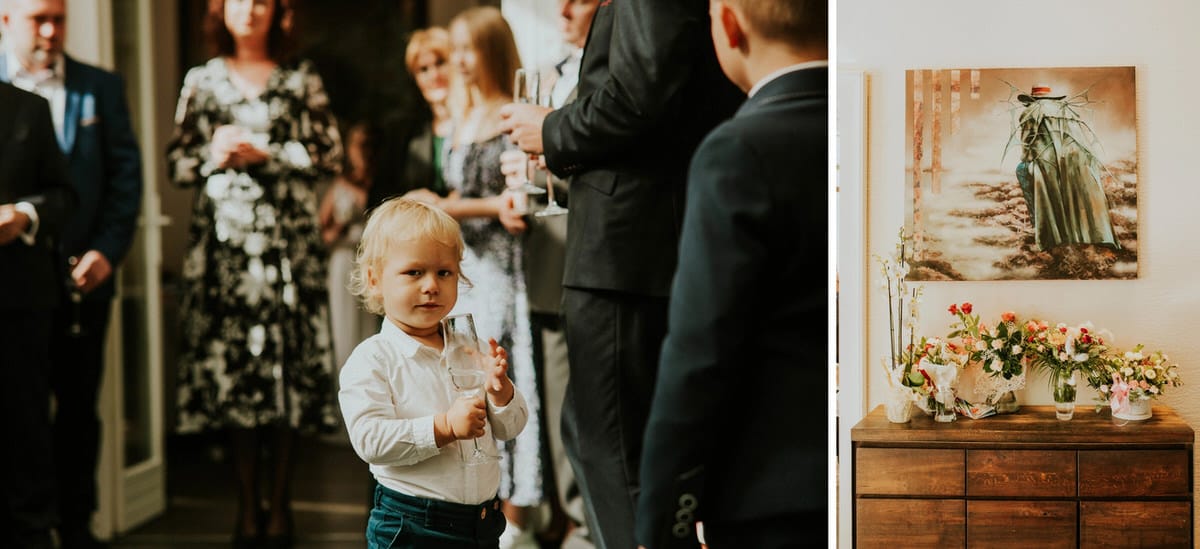 Dziecko z kieliszkiem na przyjęciu; kwiaty na komodzie.