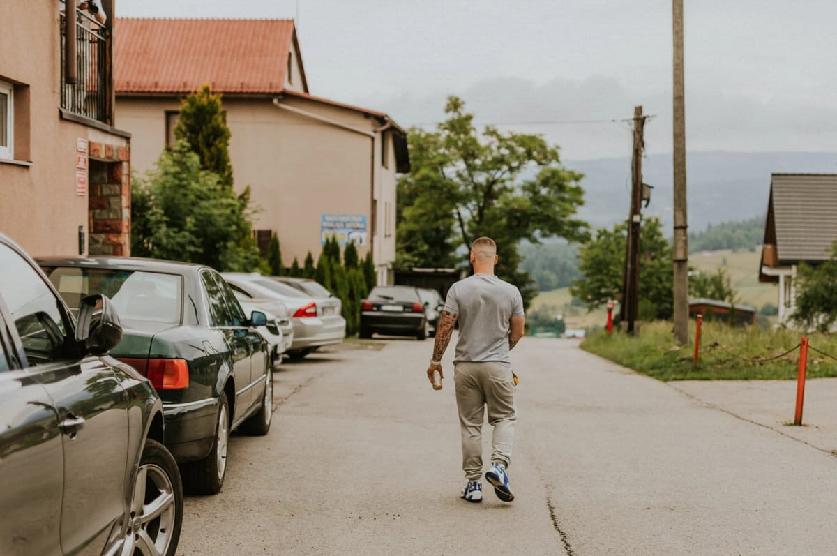 Mężczyzna idzie po wiejskiej ulicy obok zaparkowanych samochodów.