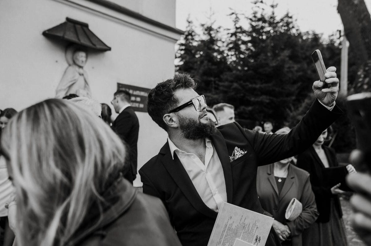 Mężczyzna robi selfie podczas uroczystości na zewnątrz.