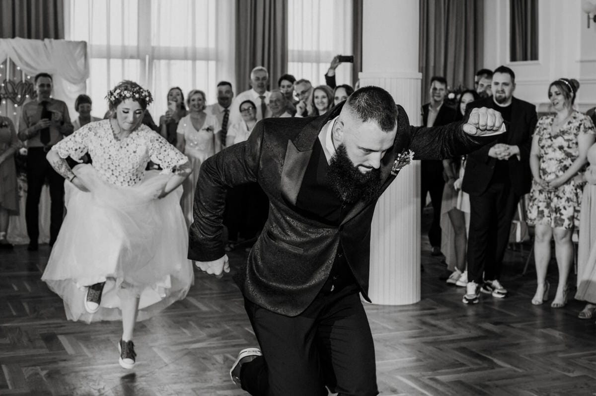 Para młoda tańczy na weselu, goście w tle.