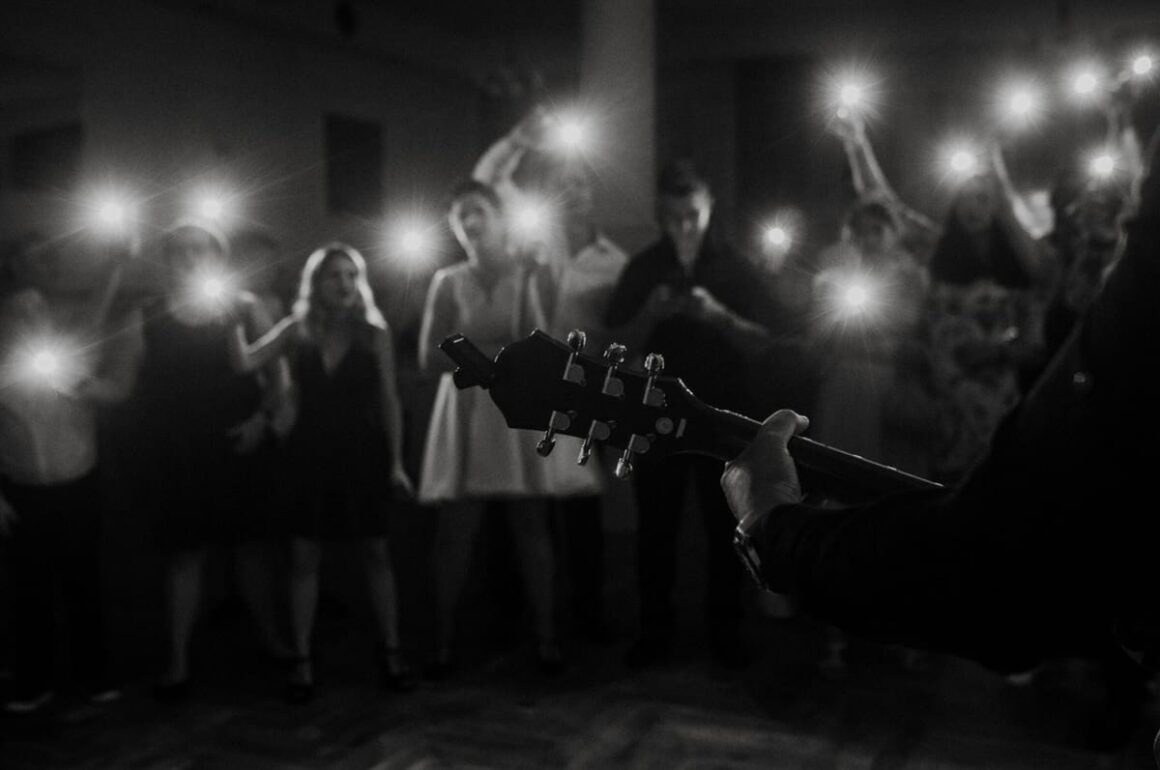Koncert, gitara w blasku świateł publiczności.