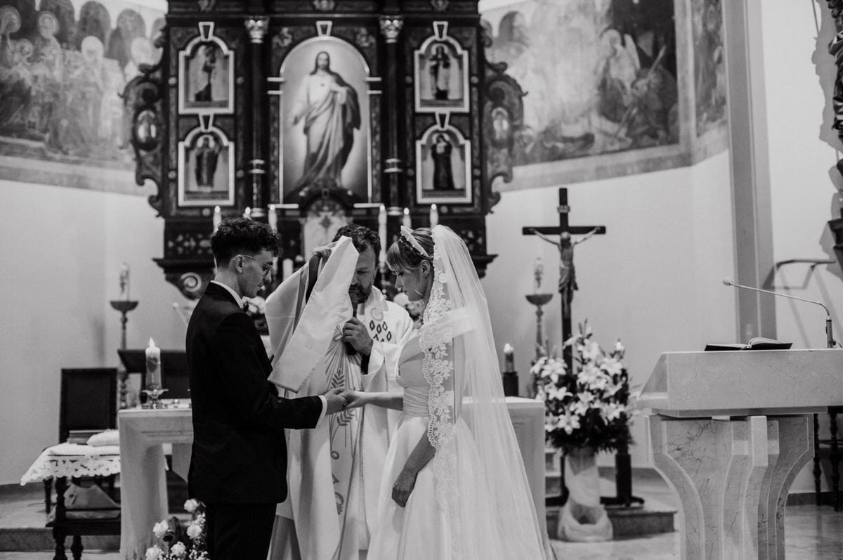 Ślub kościelny, młoda para i ksiądz przy ołtarzu.