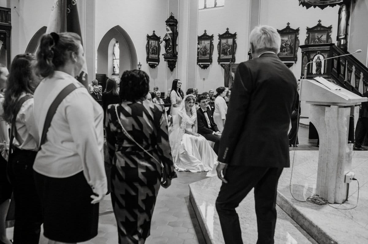 Ceremonia ślubna w kościele, młoda para siedzi.