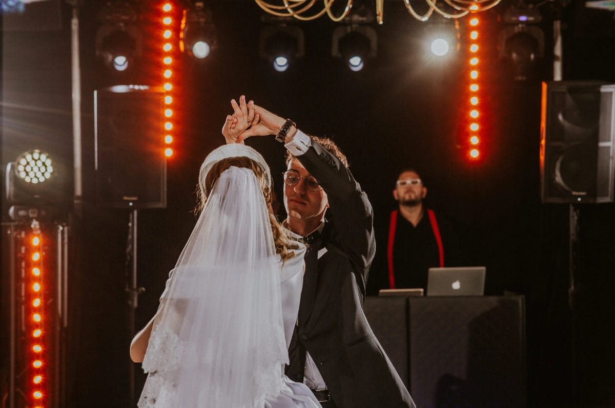 Para tańczy na weselu z DJ-em w tle.