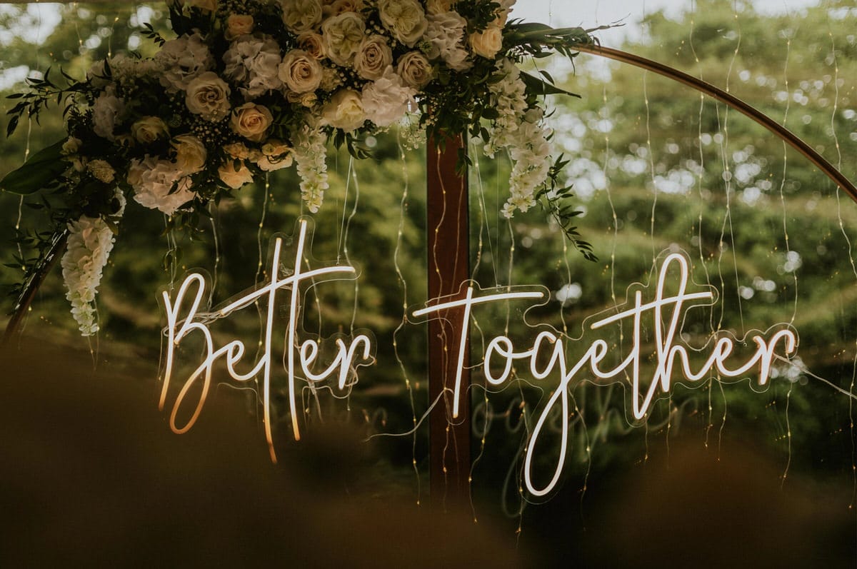 Świecący napis 'Better Together' z kwiatami w tle.