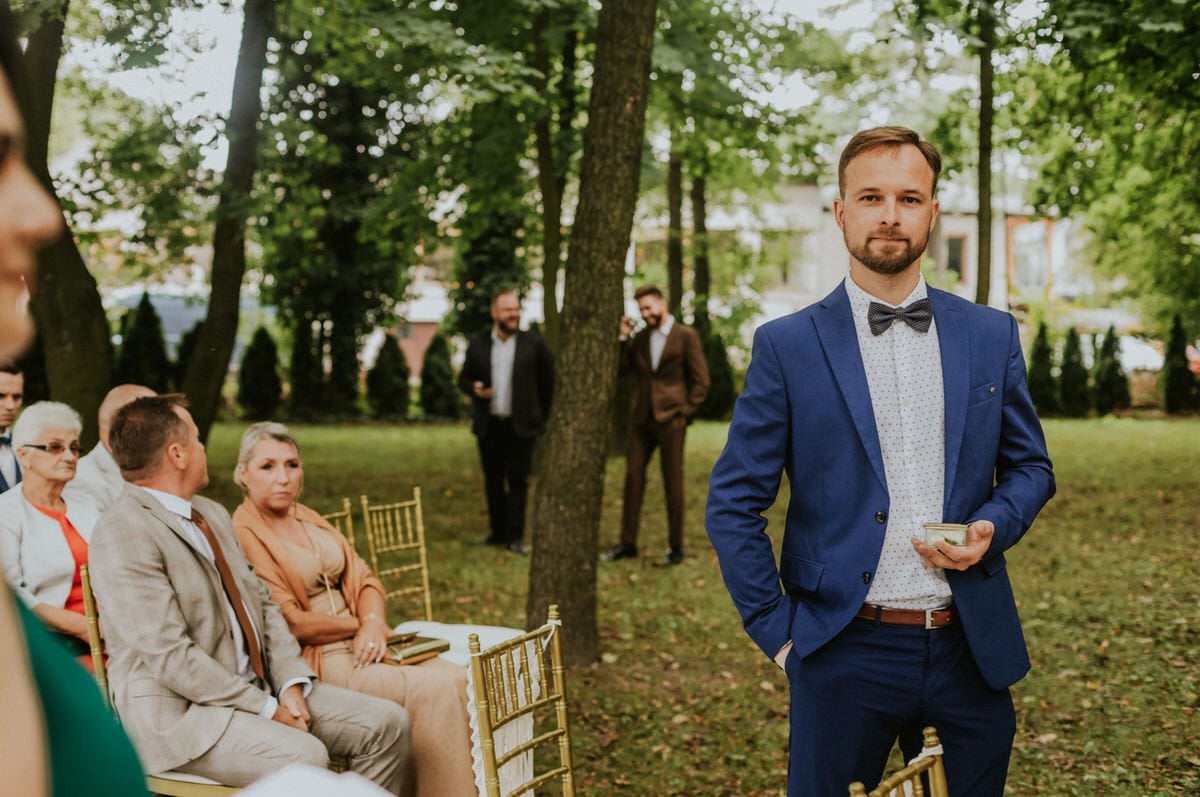 Mężczyzna w niebieskim garniturze na weselu w ogrodzie.