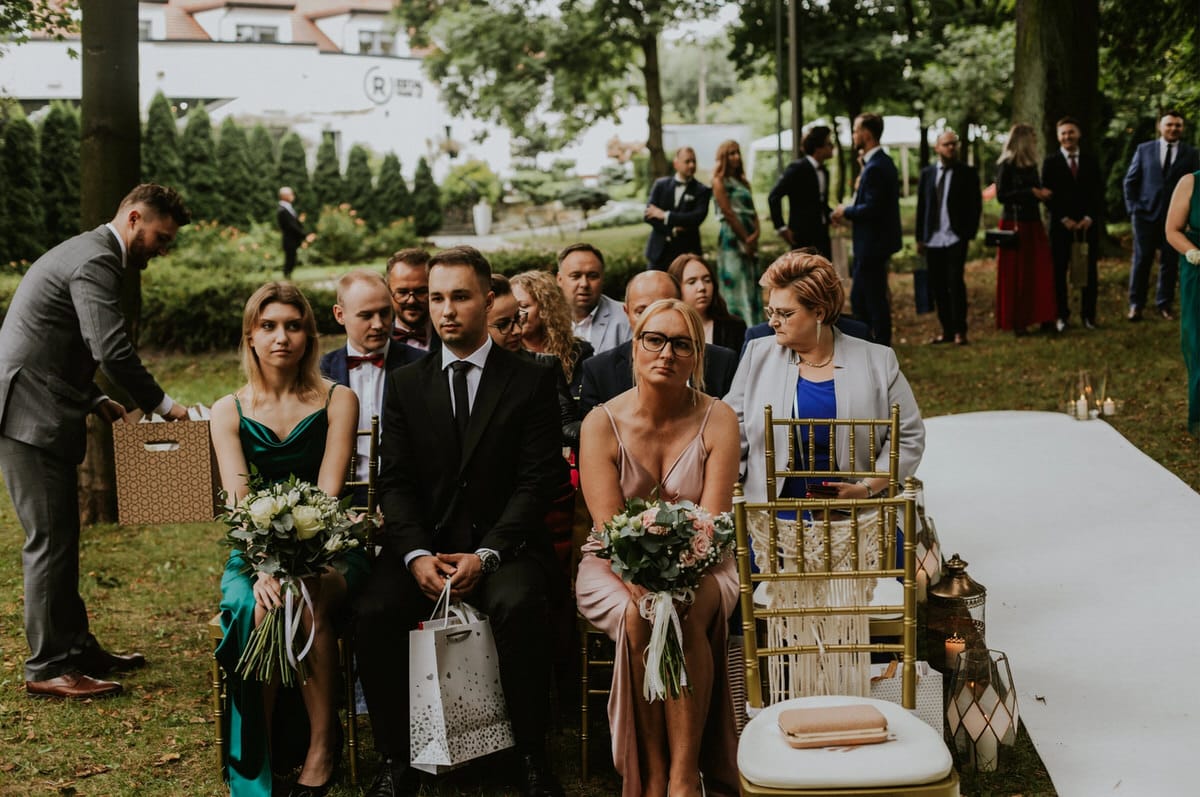 Goście weselni siedzą na zewnątrz w trakcie ceremonii.