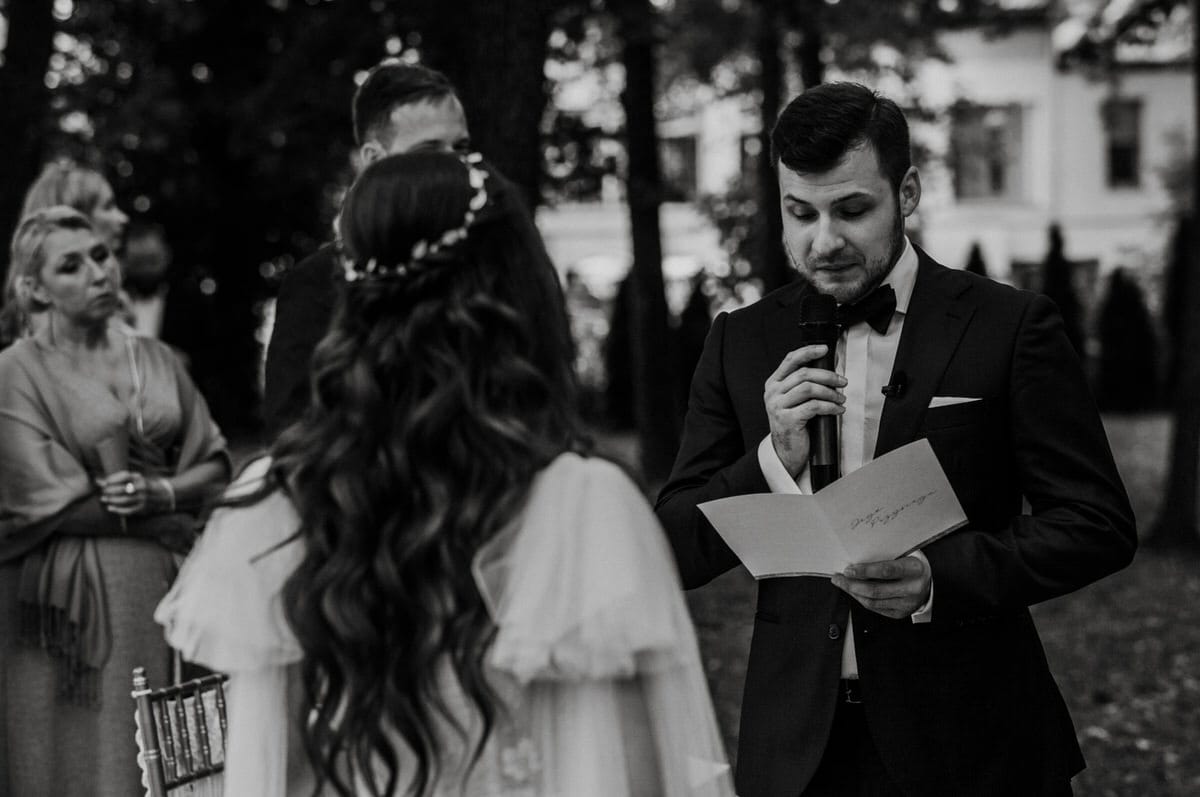 Mężczyzna przemawia na ceremonii ślubnej w ogrodzie.