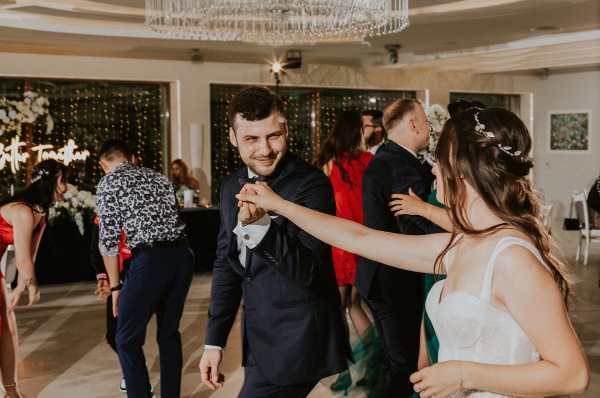Para młoda tańczy na weselu, inni goście w tle.