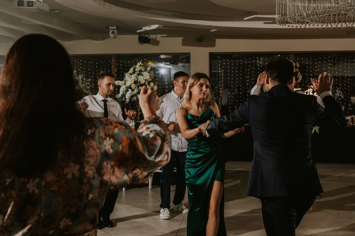 Para tańczy na weselu, eleganckie stroje, kwiaty w tle.