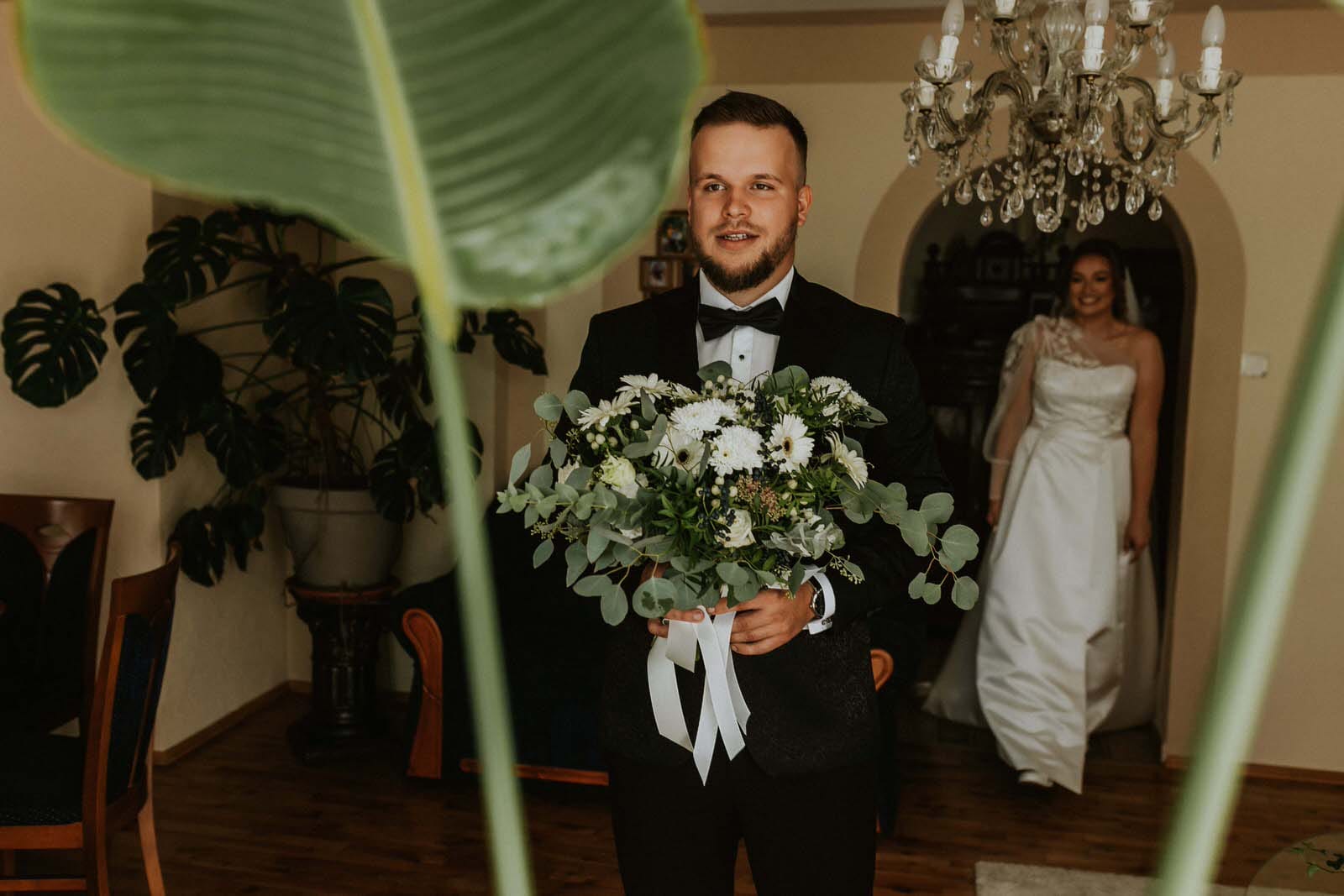 Mężczyzna z bukietem, panna młoda w tle