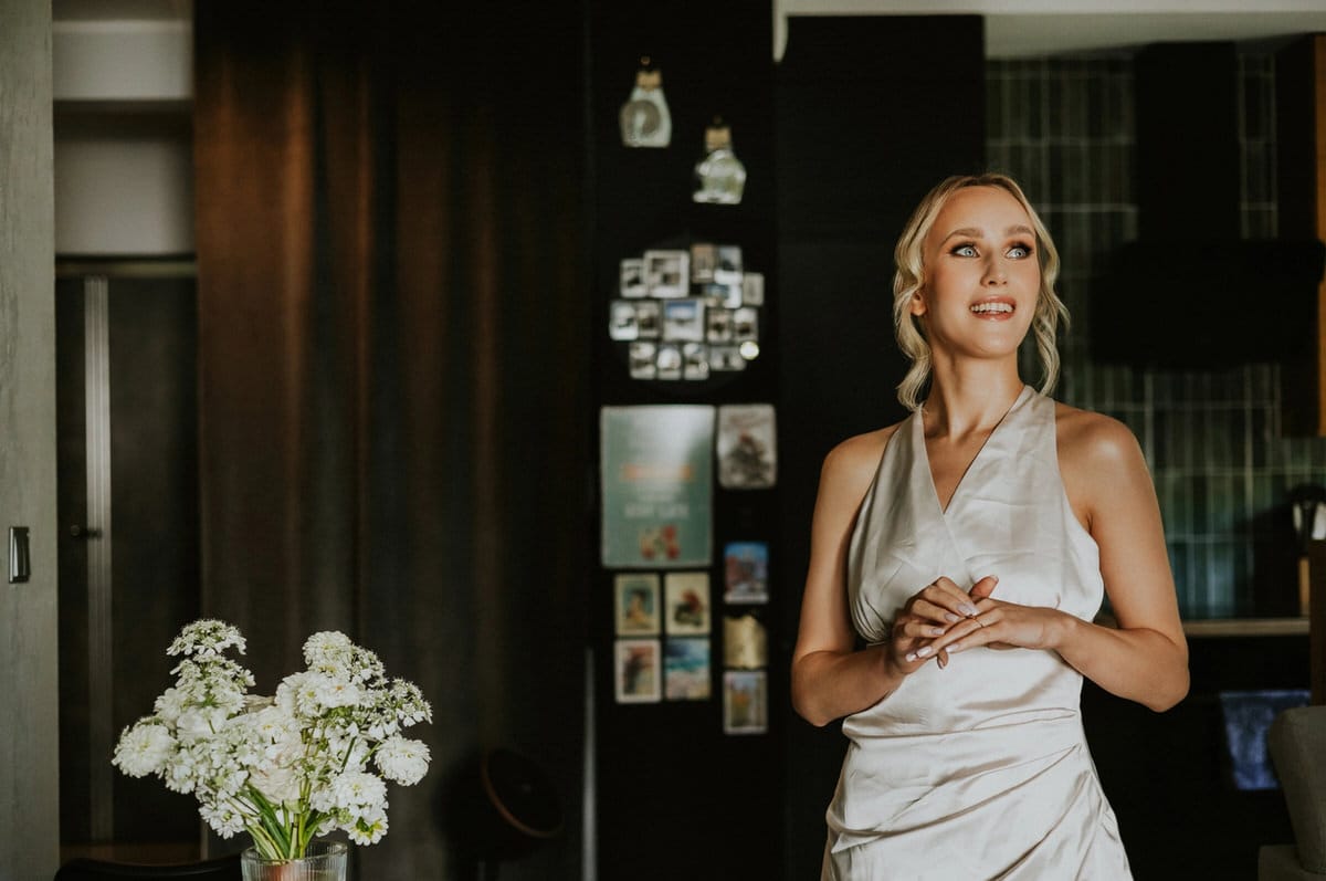Uśmiechnięta kobieta w eleganckiej sukni, kwiaty w tle.