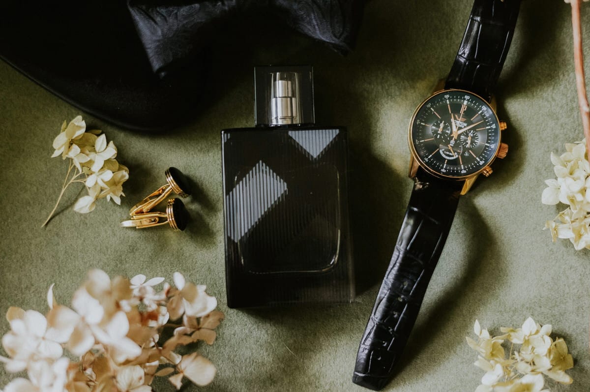 Zegarek, perfumy, spinki, kwiaty na zielonym tle.