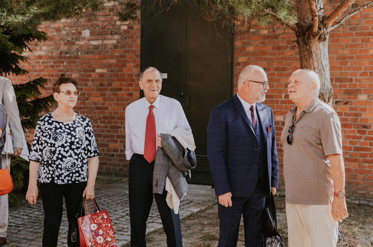 Grupa starszych ludzi rozmawia na zewnątrz koło muru.